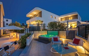 A modern two-story building with a rooftop patio area featuring a hot tub, outdoor seating, and ambient lighting. - JAZZ at Rova Apartment Lun (Malinska-Dubasnica)