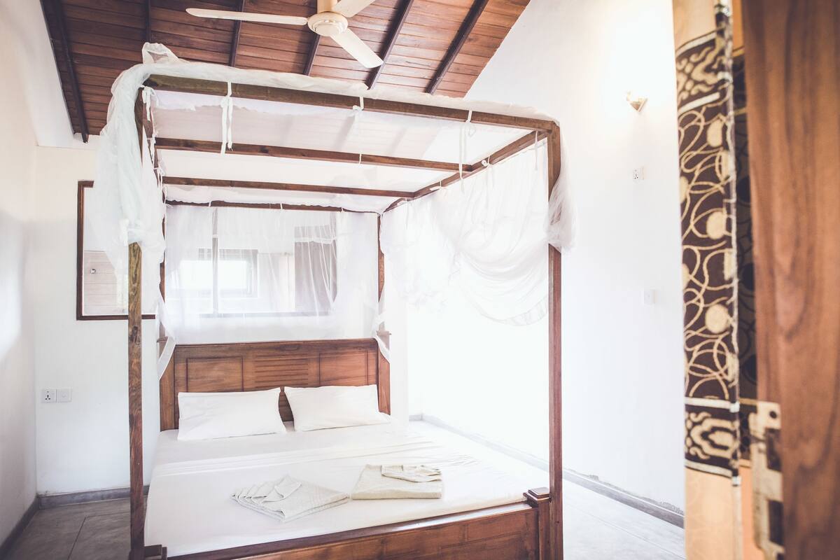 Una cama con dosel, cabecera de madera y sábanas blancas.