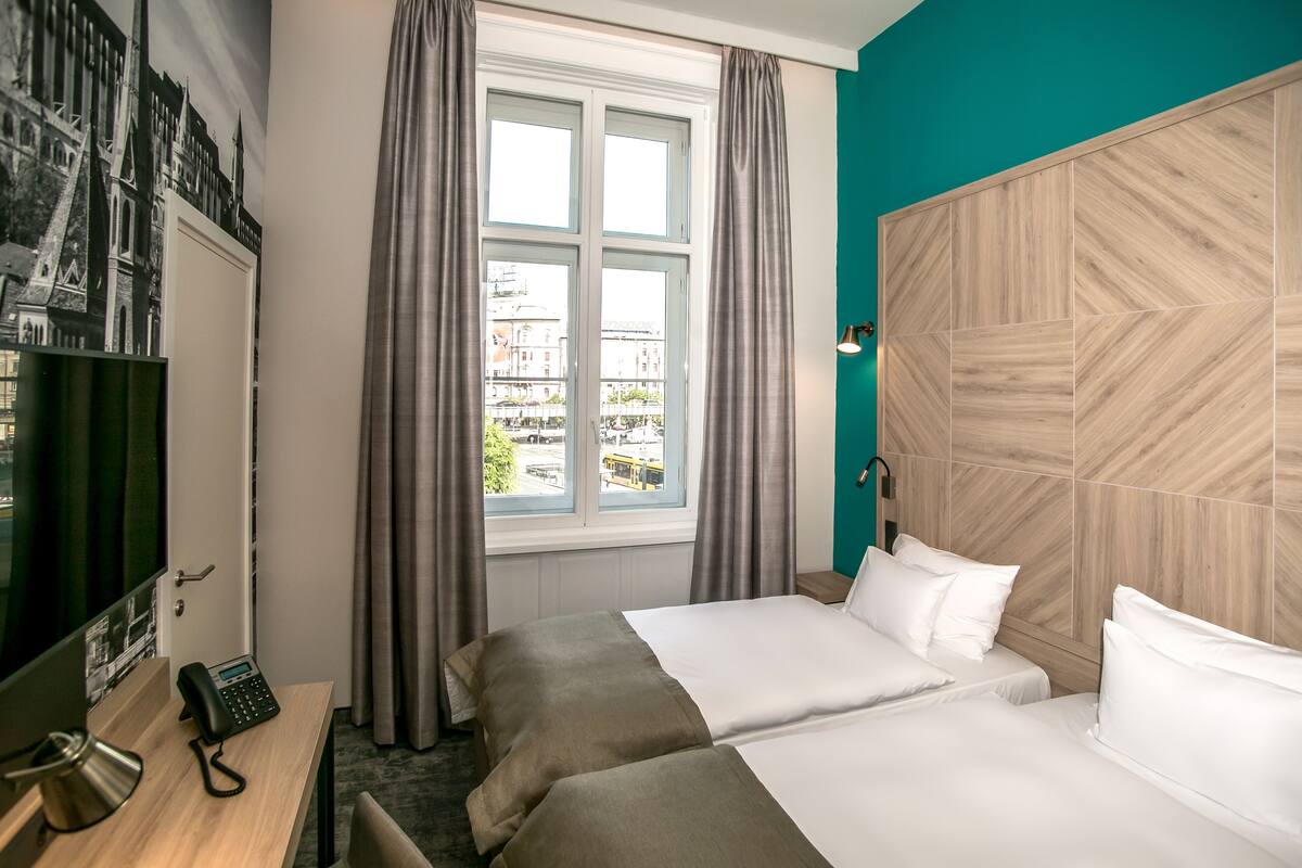 Hotellihuone, jossa on kaksi sänkyä, työpöytä, jossa on puhelin, televisio ja ikkuna, jossa on verhot.