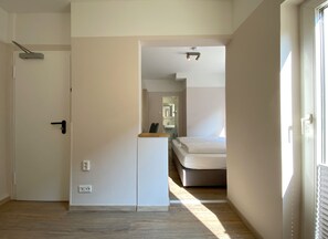 A modern hotel room with a bed, a small desk, a mirror, and a door leading to another room. - Also-hotel an der Hardt (Wuppertal)