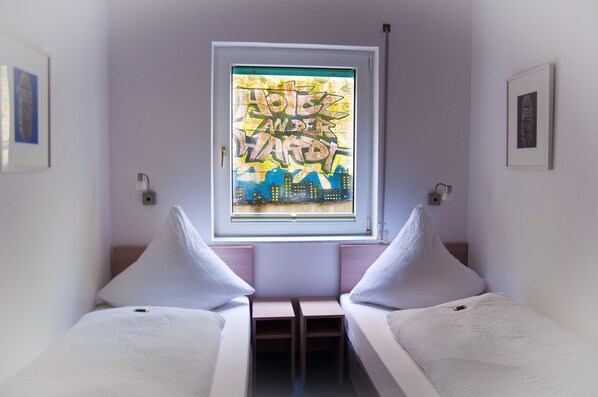A small, single-bed room with a window featuring a colorful graffiti artwork. - Also-hotel an der Hardt (Wuppertal)