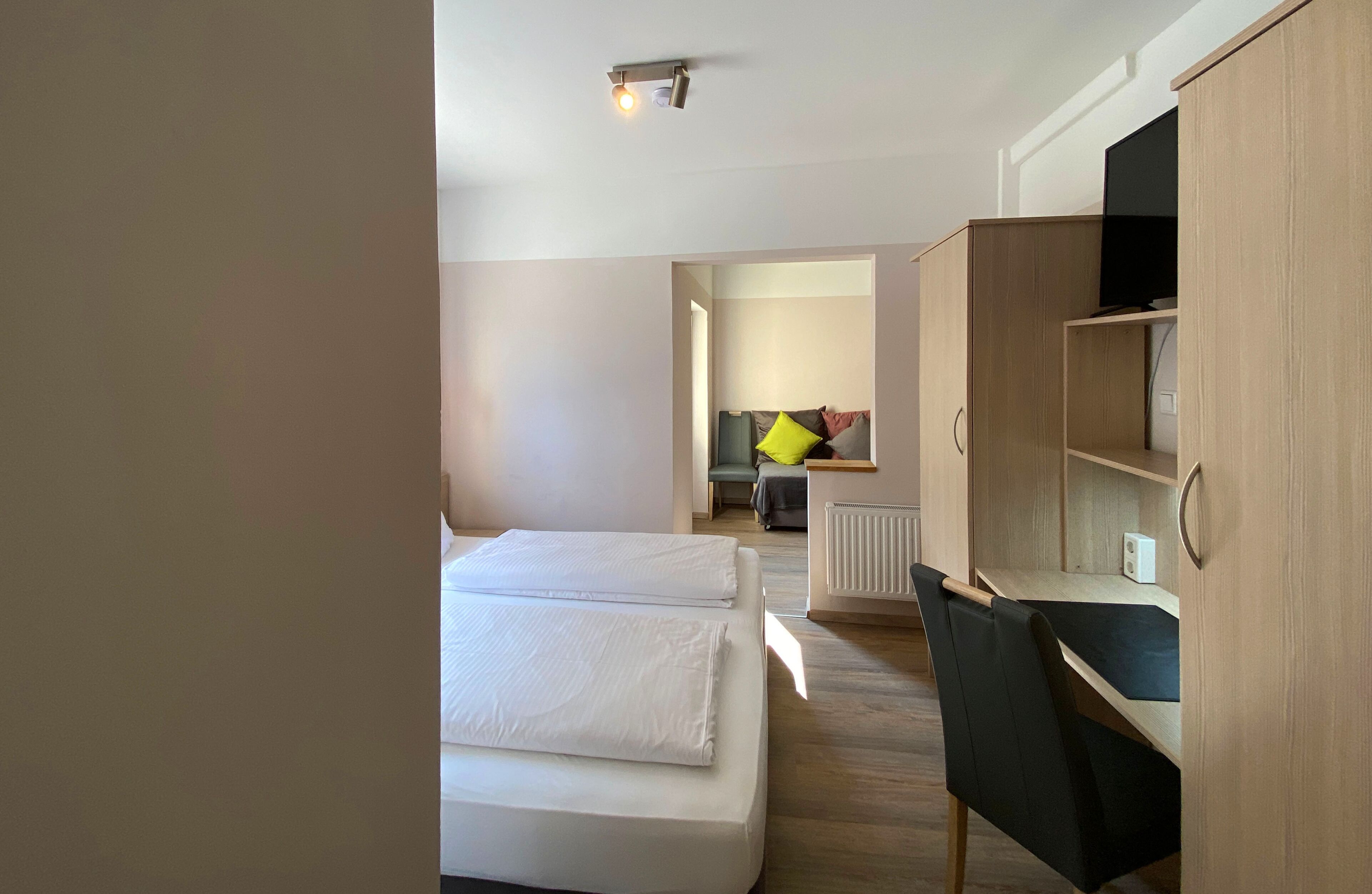 A hotel room with a bed, a desk, and a chair. There is a television on a wooden cabinet.