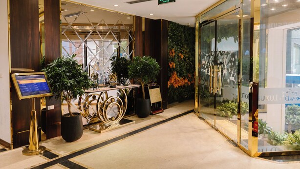 Um hall de hotel com balcão de recepção, plantas em vasos, parede de vidro com vista e placa indicando a saída.