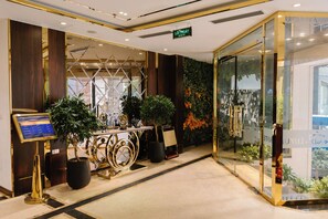 A hotel lobby with a reception desk, potted plants, a glass wall with a view, and a sign indicating the exit. - A&D Luxury Hotel (Hanoi)