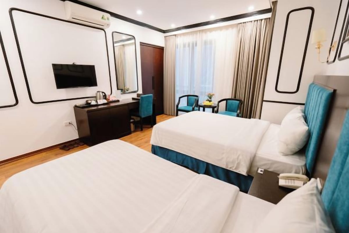 A hotel room with two beds, a desk, a TV, and a window with curtains.