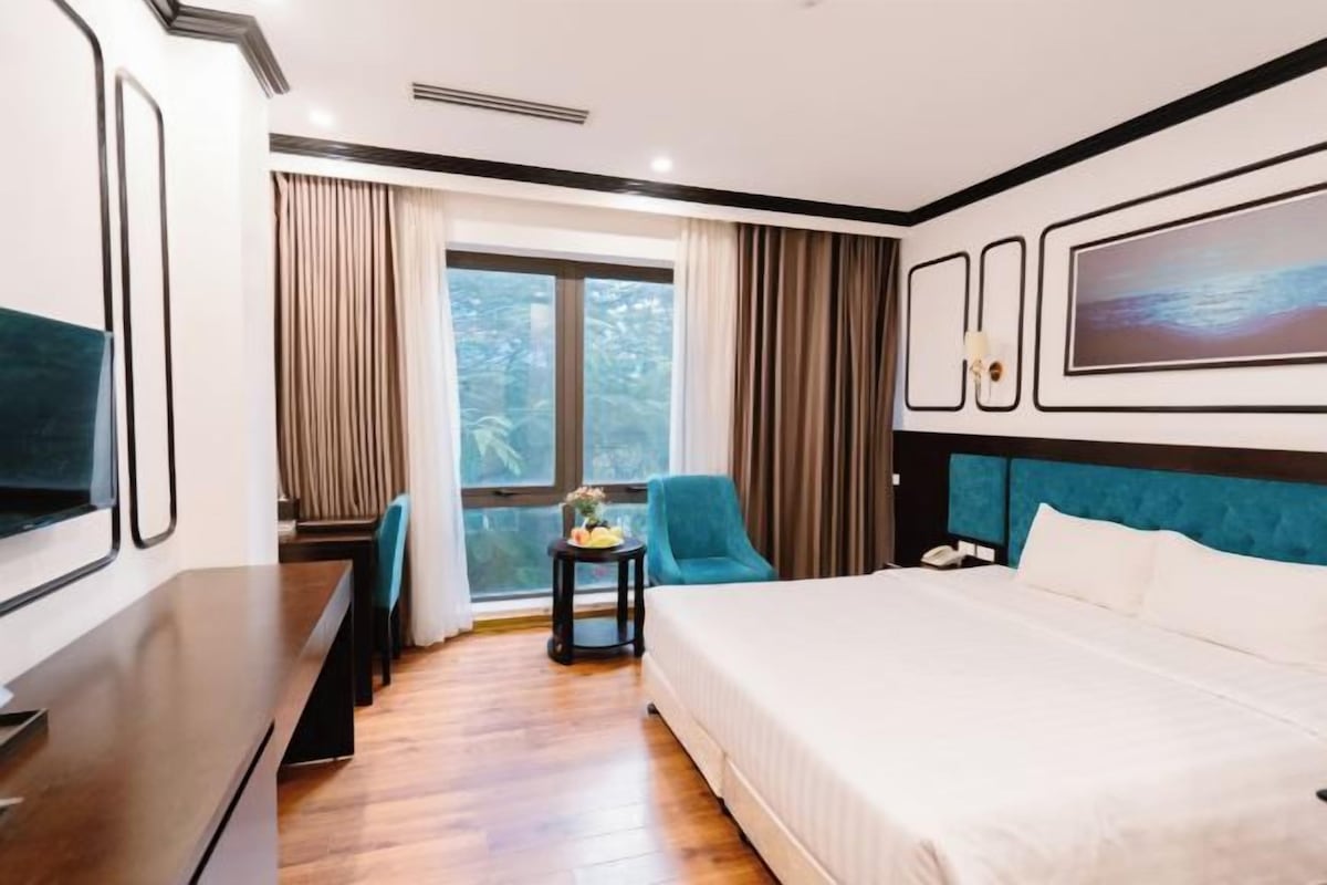 A hotel room with a large bed, a desk, a chair, and a window with curtains.