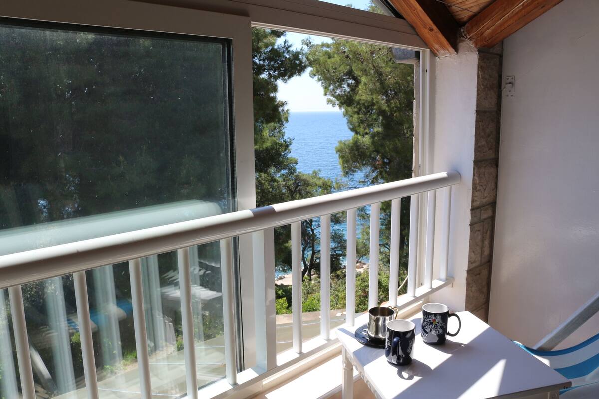 A balcony with a view of the sea, a white railing, and two mugs on a table.