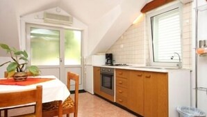 A compact kitchen with a stove, oven, and a coffee maker on the countertop. There is a window with blinds, a sink, and a trash bin. - Apartmani Ančila (Smokvica)