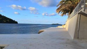 A paved walkway leading to a beach with a clear view of the sea and distant islands. - Apartmani Ančila (Smokvica)