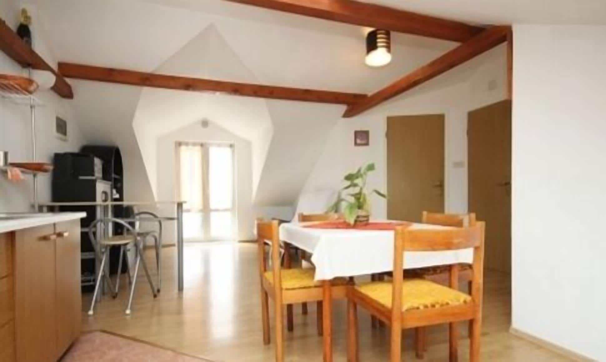 Uma área de refeições com mesa e cadeiras, teto com vigas de madeira e uma cozinha com fogão e armários.