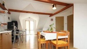 A dining area with a table and chairs, a ceiling with wooden beams, and a kitchen area with a stove and cabinets. - Apartmani Ančila (Smokvica)