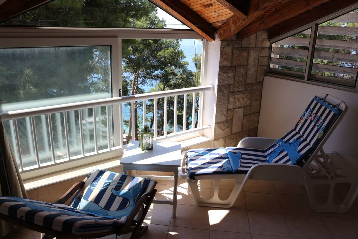 A balcony with two sun loungers, a table, and a view of the sea.