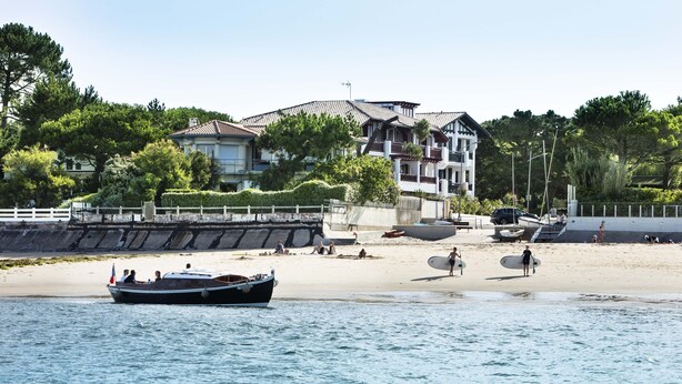 Un paysage côtier avec une plage, un bateau et un grand bâtiment doté de nombreux balcons.
