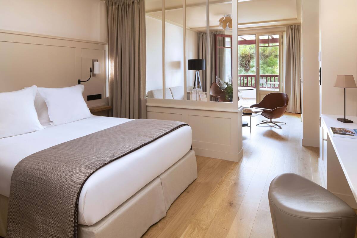 Ein Hotelzimmer mit einem großen Bett, einem Schreibtisch, einem Sessel und Blick ins Freie.