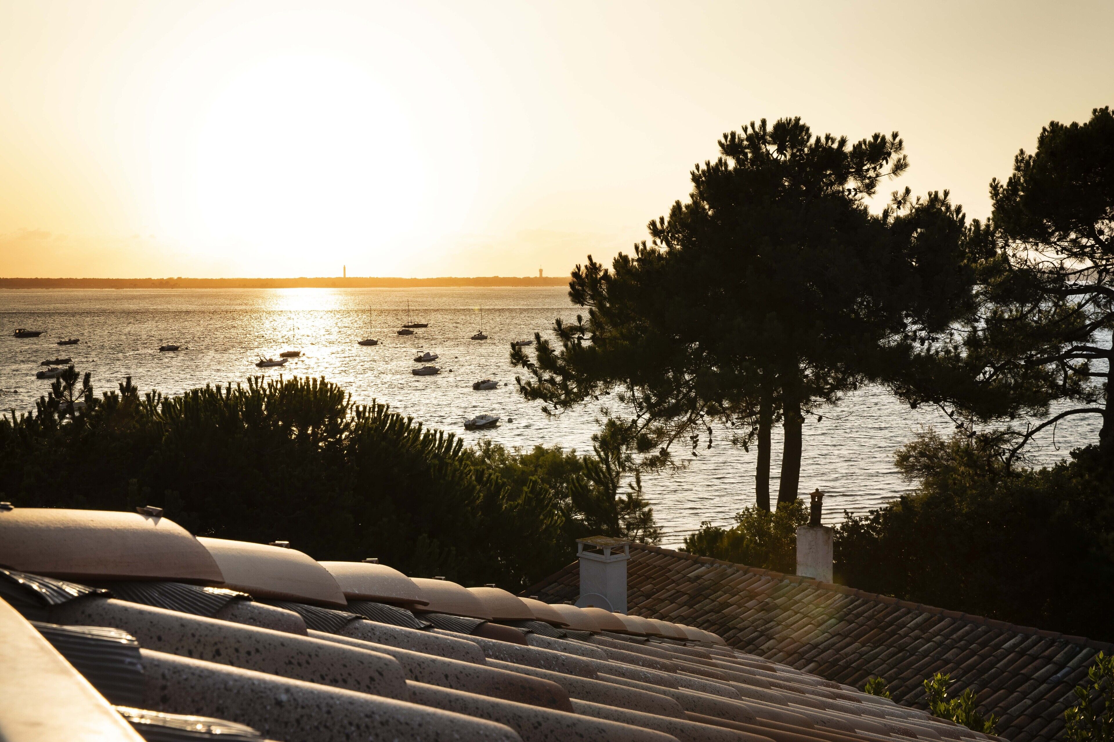 A coastal view with boats on the water, a tree, and a building with a tiled roof.