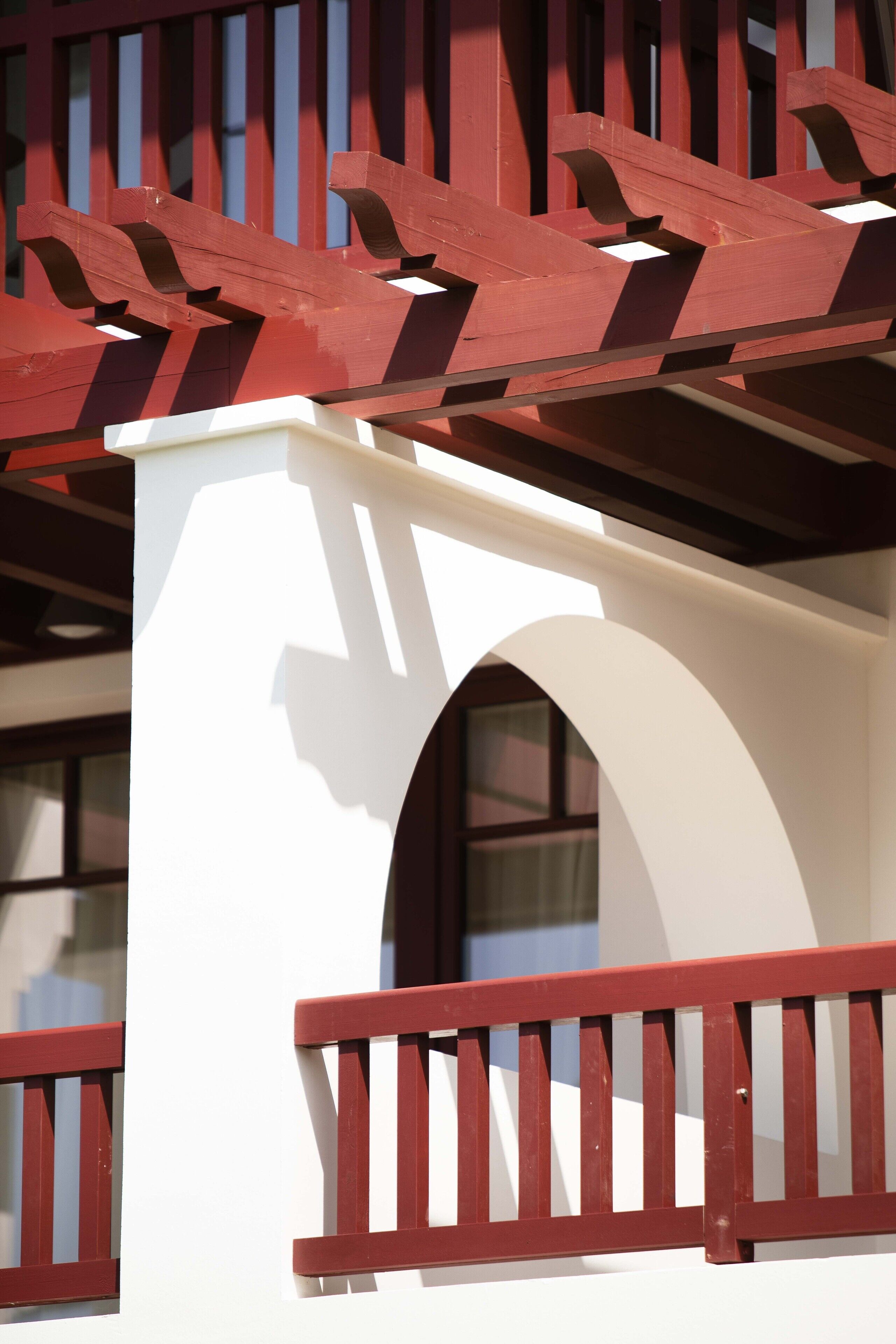 Un bâtiment à la façade blanche et aux éléments décoratifs rouges, doté d’un balcon avec une balustrade rouge.