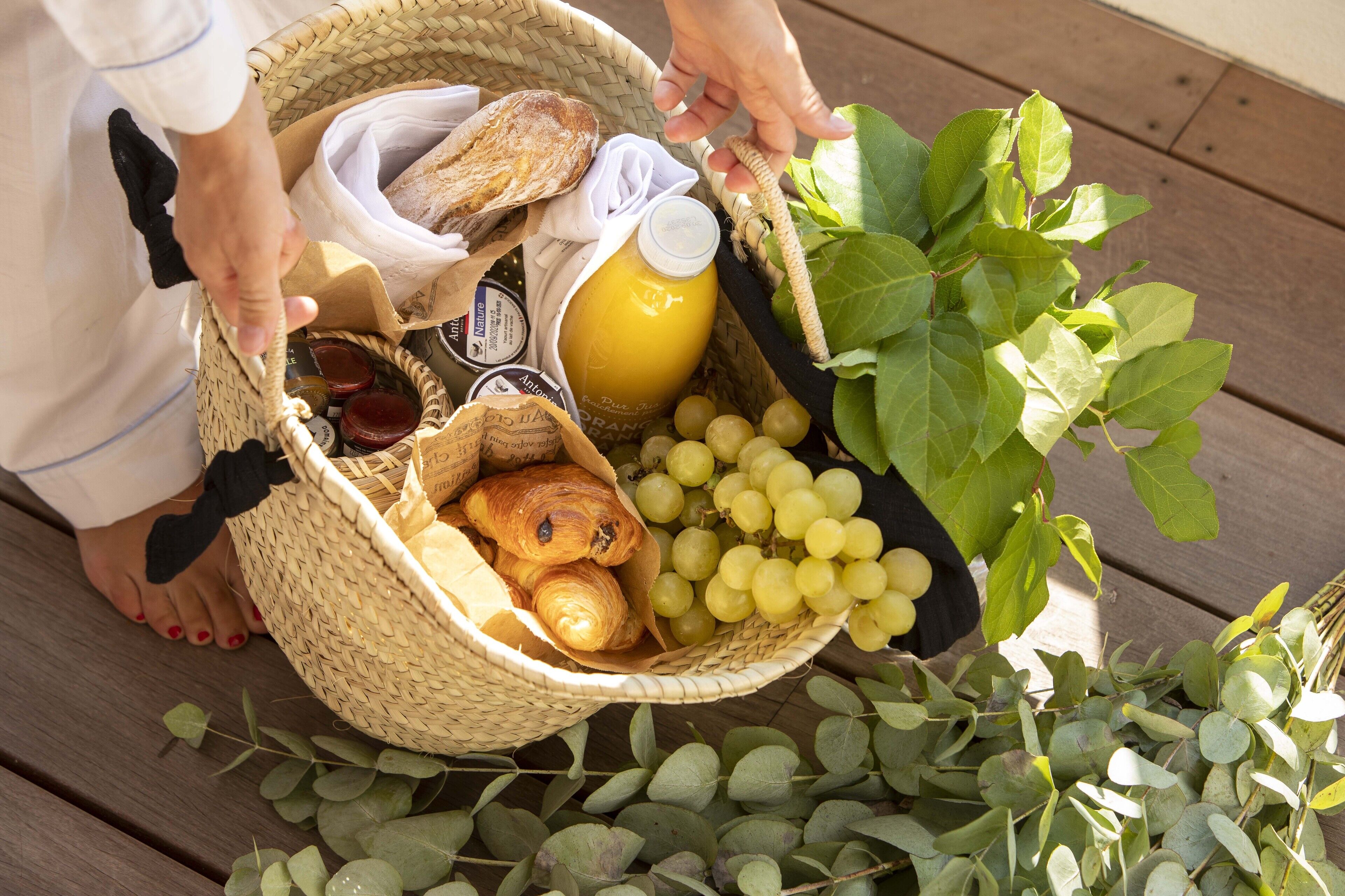 Una cesta de mimbre llena de alimentos, como pan, uvas y una botella de jugo, sobre una superficie de madera.