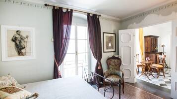 Een slaapkamer met een bed, een stoel, een bureau en een deur naar een andere kamer.