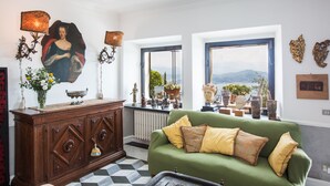 A living room with a green sofa, wooden cabinet, and a large window with a view of the sea. - Villa Cà Mea (La Spezia)