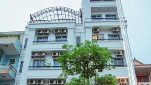 A multi-story hotel with a prominent entrance, air conditioning units, and a tree in front. - Rosavila (Phan Dinh Phung)