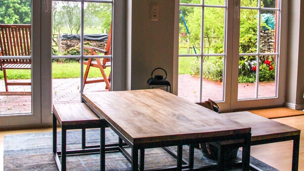 A room with a wooden table and benches, large sliding glass doors leading to a garden. - Ferienapartments Lüneburger Heide - Rehlingen (Rehlingen)
