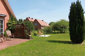 A brick house with a red roof, a wooden deck, and a well-maintained lawn.