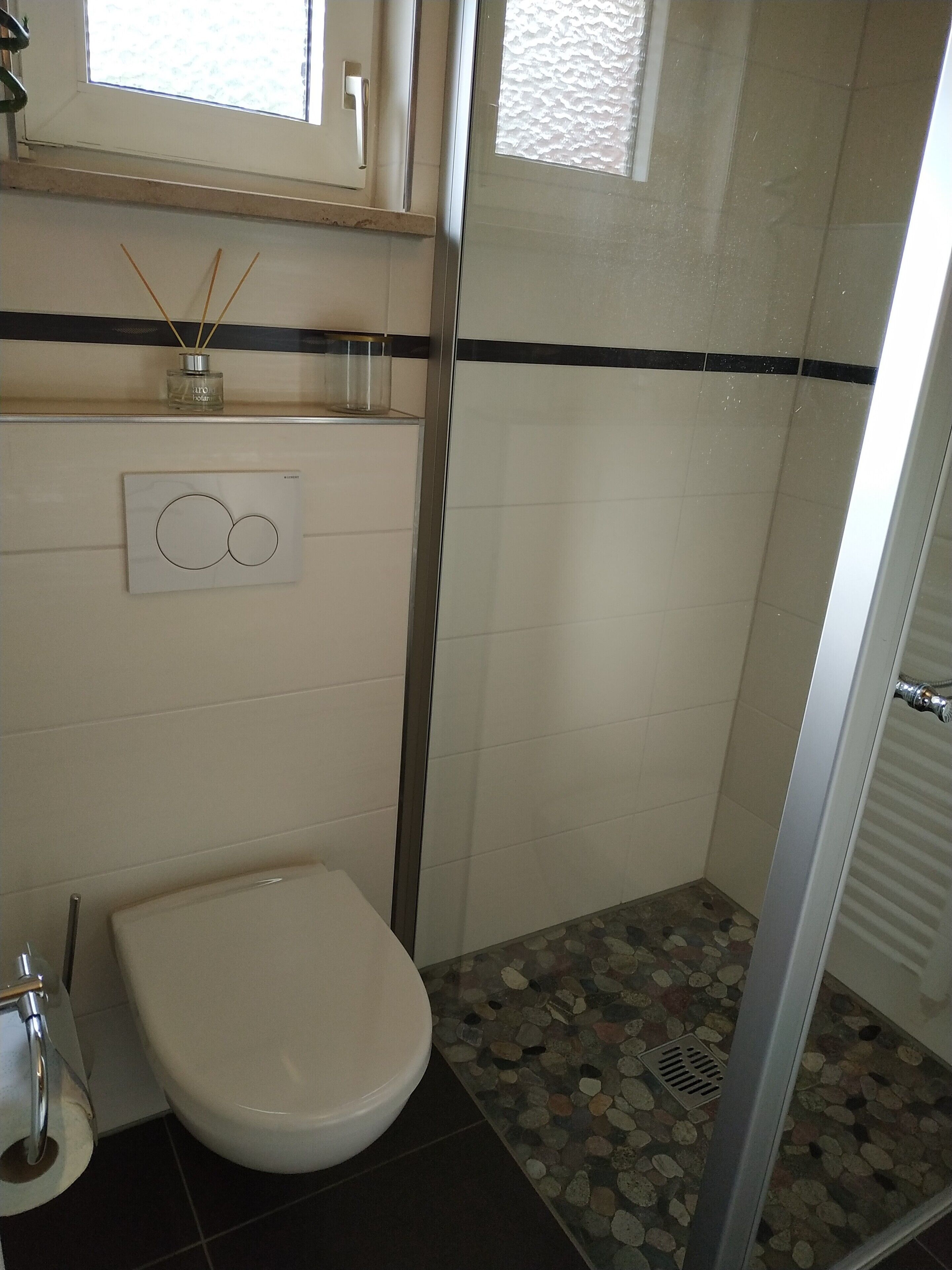 A bathroom with a toilet, a shower with a tiled floor, and a window with a textured glass panel.
