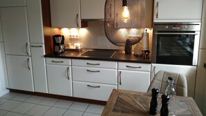 A modern kitchen with white cabinets, a black countertop, a wooden dining table, and a hanging light fixture. - Ferienapartments Lüneburger Heide - Rehlingen (Rehlingen)