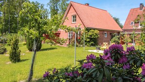A red-brick house with a tiled roof, surrounded by a well-maintained garden with grass and flowering plants. - Ferienapartments Lüneburger Heide - Rehlingen (Rehlingen)