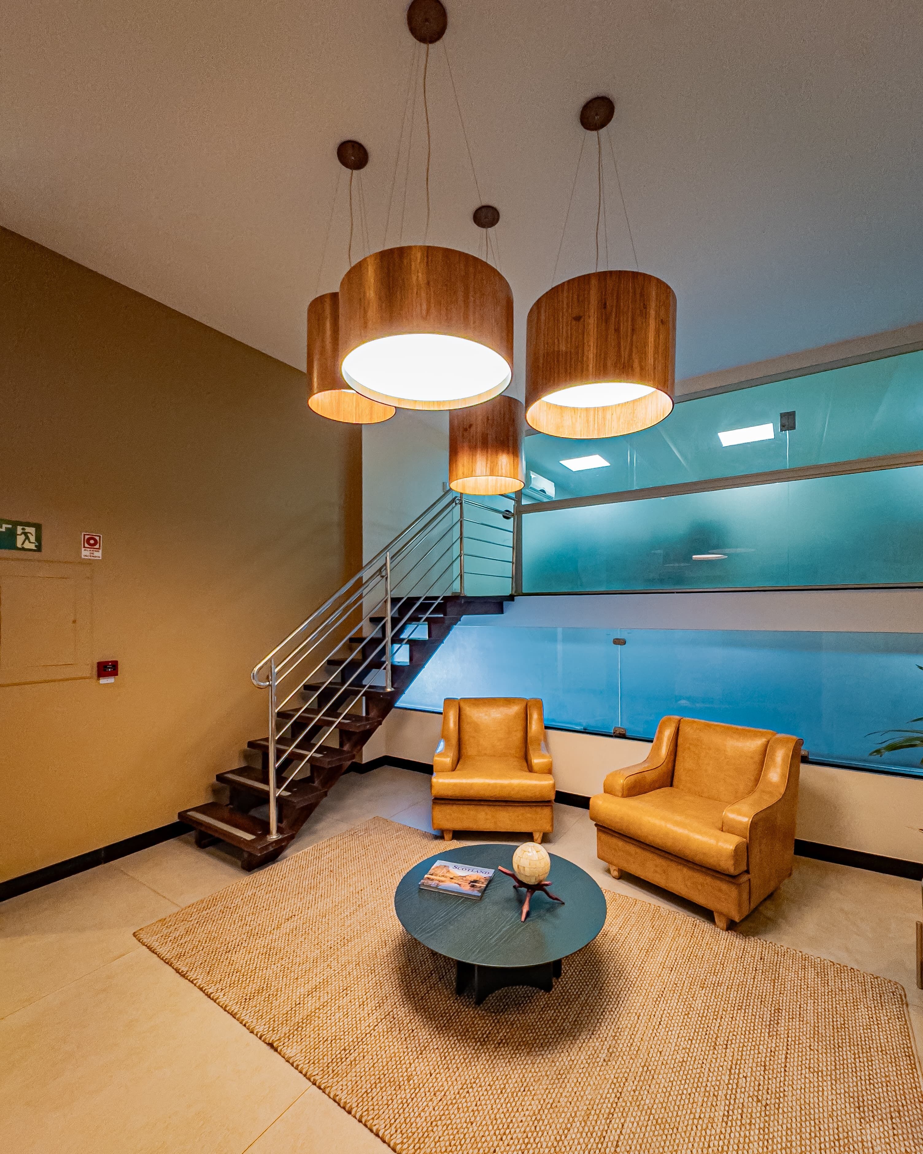 Un vestíbulo con una escalera, sillones de cuero, una mesa de centro con un globo terráqueo y lámparas colgantes de madera.