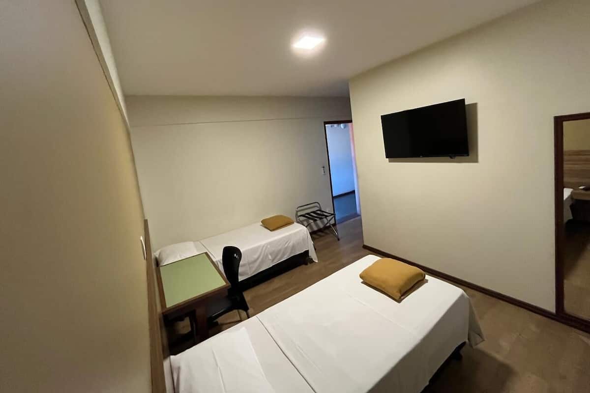 A hotel room with two single beds, a desk, a chair, a flat-screen TV mounted on the wall, and a door leading to another room.