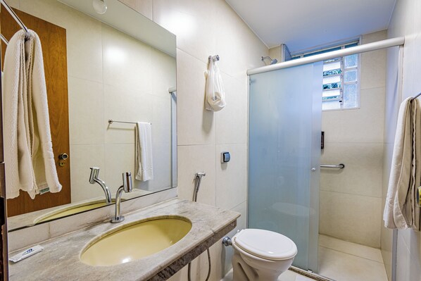 Baño con lavamanos, espejo, inodoro y cabina de ducha de vidrio.
