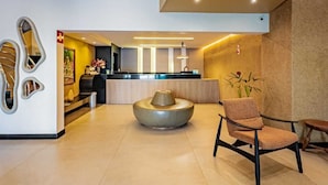Un vestíbulo moderno con una mesa de recepción, una zona de estar con una mesa redonda y un elemento decorativo en la pared.