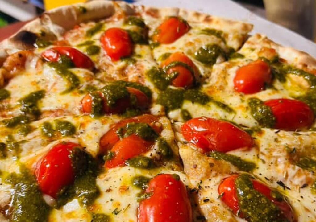 A pizza with cheese, tomatoes, and green sauce.