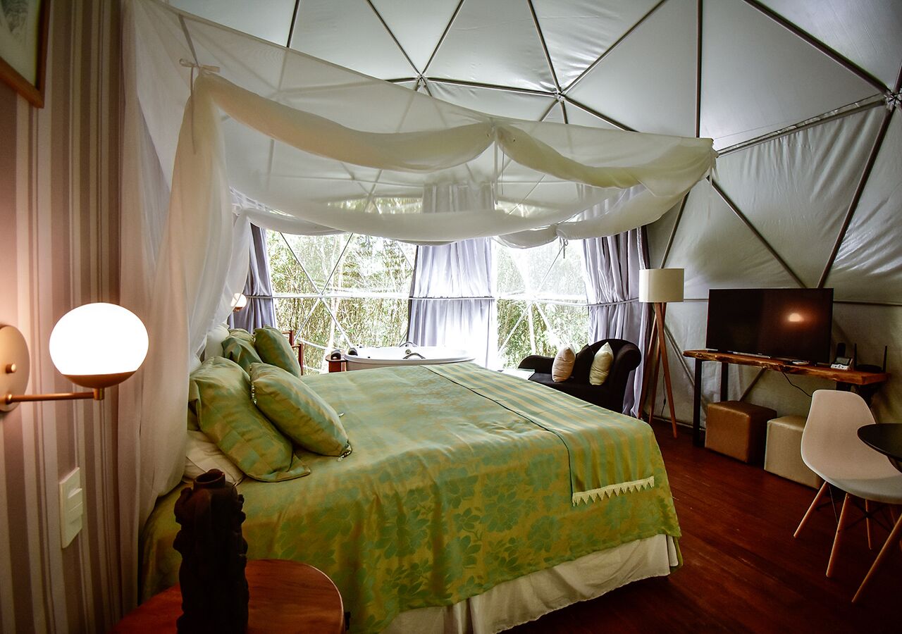A tented room with a bed, a desk, a chair, and a television.