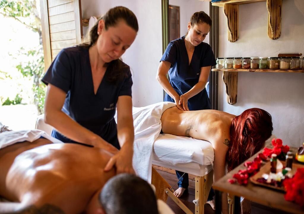 A massage therapy session in a room with wooden shelves and jars.