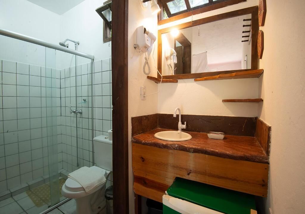 A bathroom with a glass shower enclosure, a toilet, a sink with a wooden countertop, and a mirror with a wooden frame.