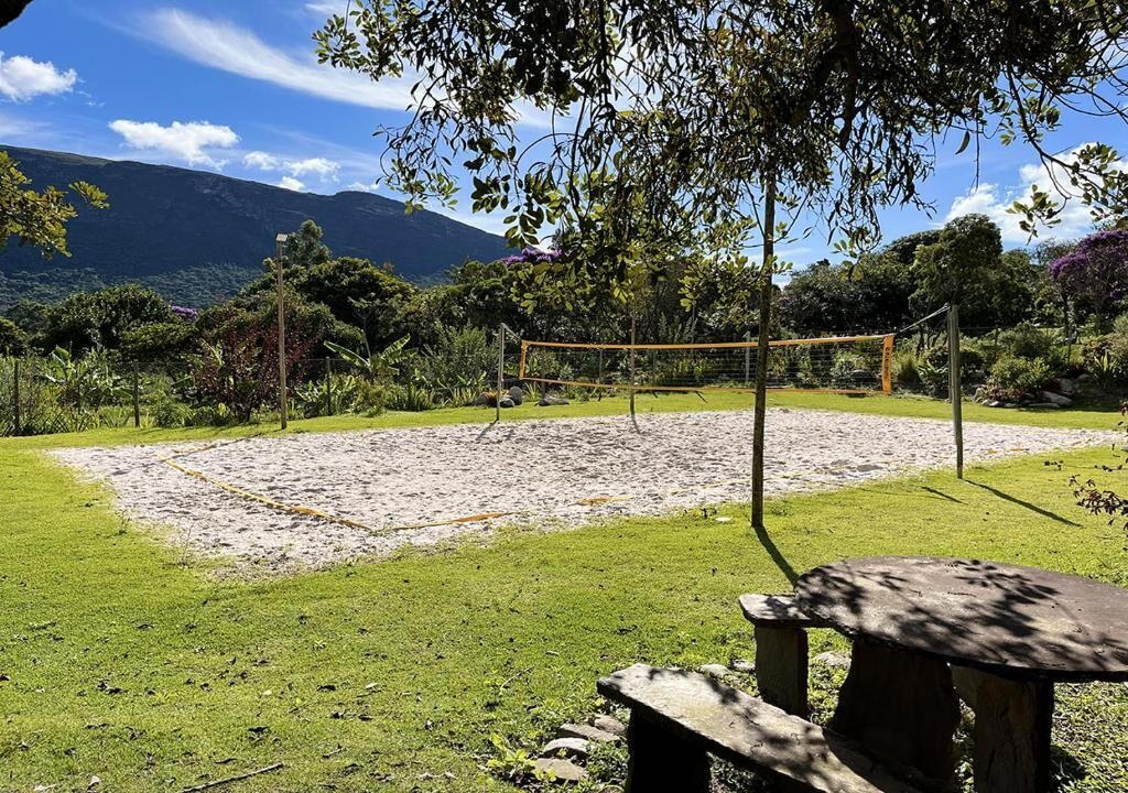 A volleyball court with a net, surrounded by a grassy area and trees.