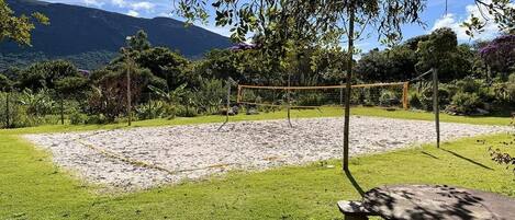 A volleyball court with a net, surrounded by a grassy area and trees.