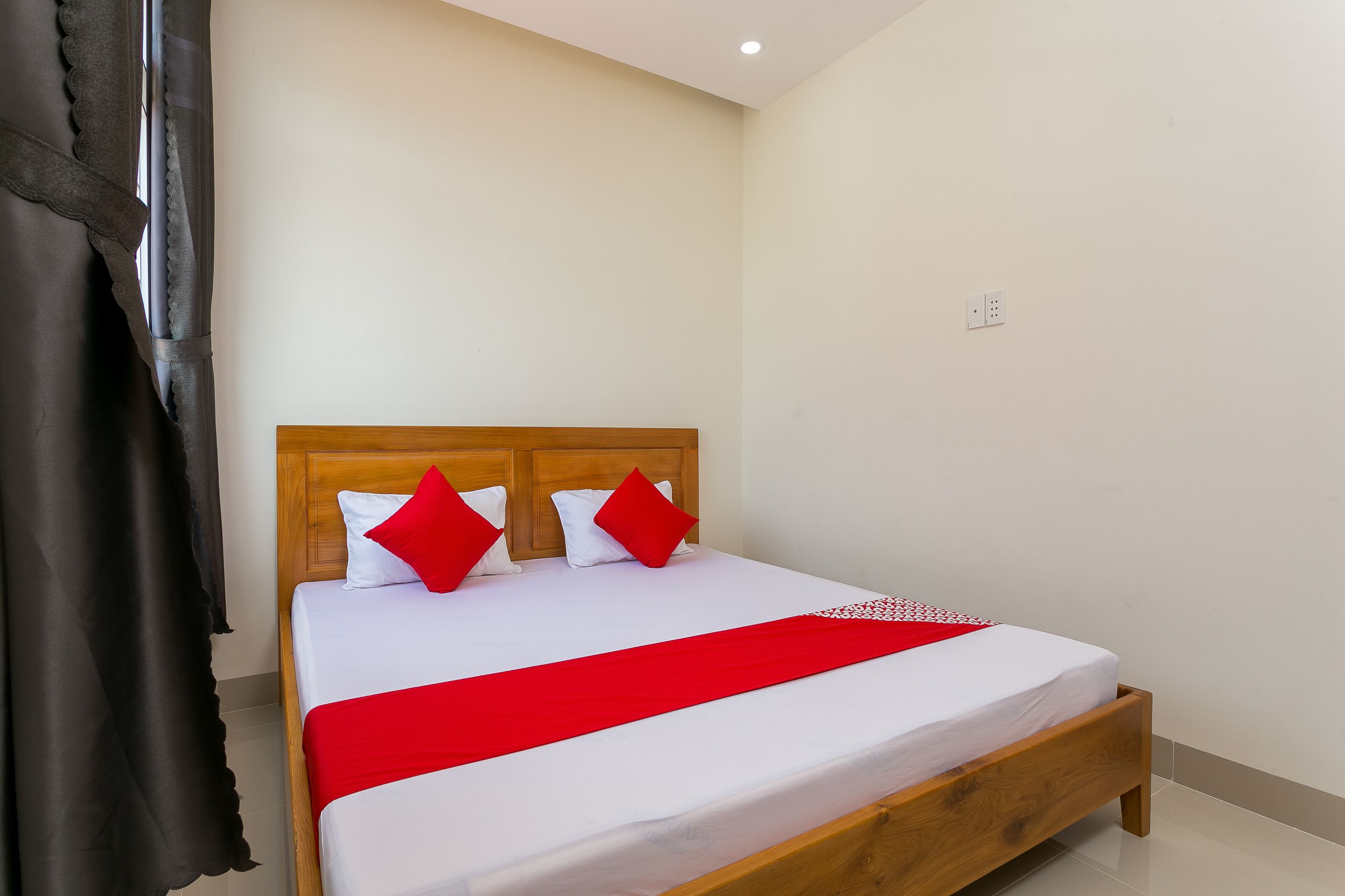 A neatly made bed with a wooden headboard, white bedding, and red accents.