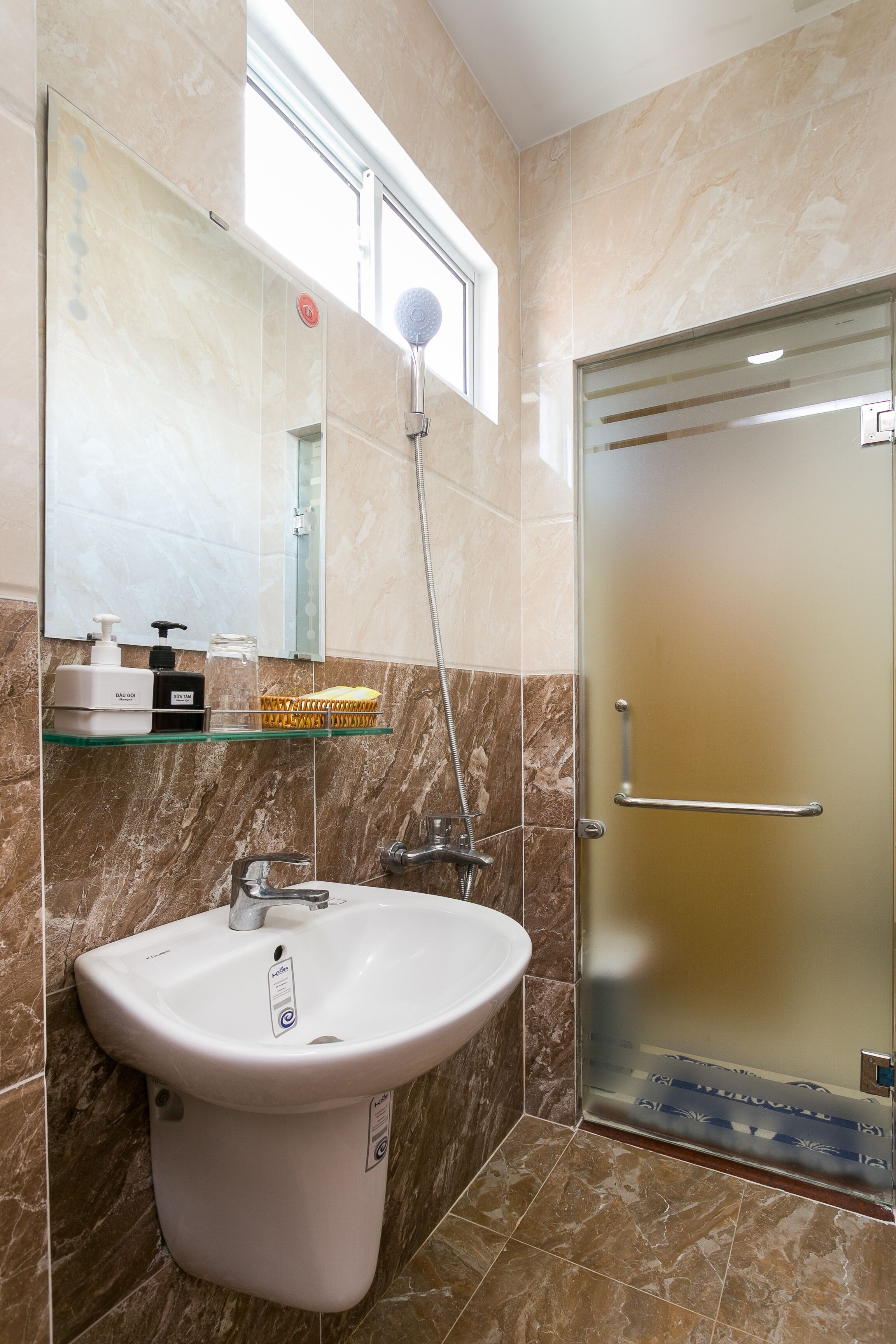 A bathroom with a white sink, a glass shower enclosure, and a marble-tiled wall.