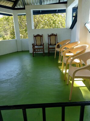 A covered outdoor area with green flooring, two wooden chairs with woven backs, and wicker chairs.