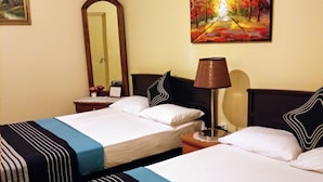 A hotel room with two beds, a nightstand with a lamp, a painting on the wall, and a mirror. - Windsor Forest Bungalow (Bandarawela)
