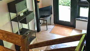 A room with a wooden staircase, a television on a stand, a small table, and a door leading outside. - Ferienapartments Lüneburger Heide - St. Dionys (Barum)