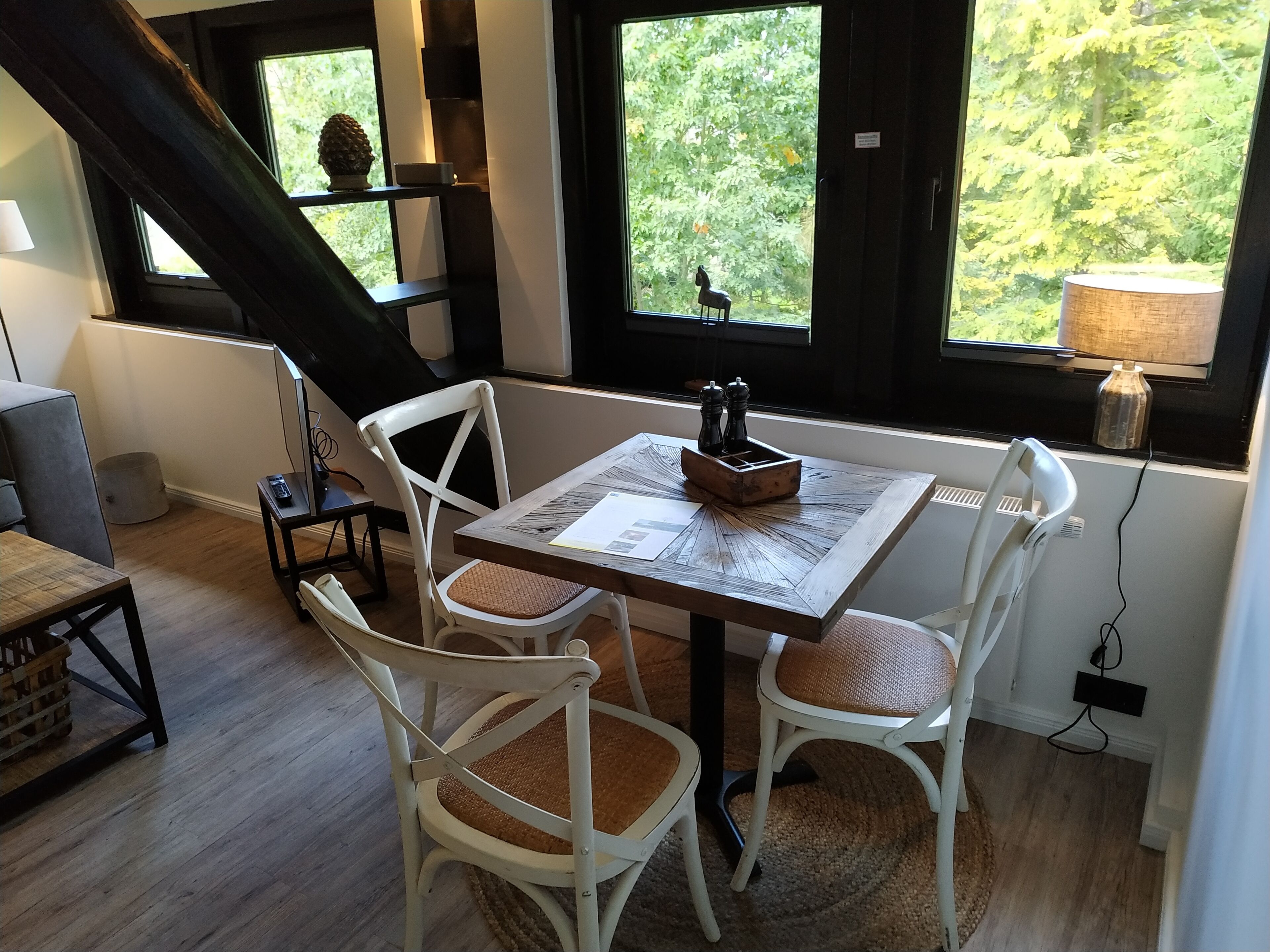 Un comedor acogedor con una mesa de madera, sillas blancas y vistas a la vegetación a través de amplios ventanales.