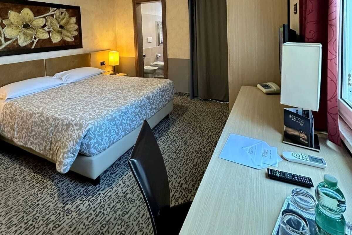 Una habitación de hotel con cama, escritorio y ventana con cortinas.