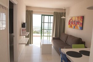 Una sala moderna con un sofá, una mesa de centro y una mesa de comedor. Hay un ventanal con cortinas, un cuadro en la pared y vistas al exterior.