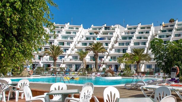 Un complexe hôtelier doté d’une piscine, de bâtiments blancs et de palmiers.