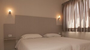 Une chambre à coucher avec un grand lit, deux lampes fixées au mur, une table de chevet et une fenêtre avec des rideaux.