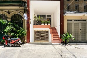 Entrada residencial con una escalera que lleva a un segundo piso, plantas en macetas y una motocicleta estacionada.